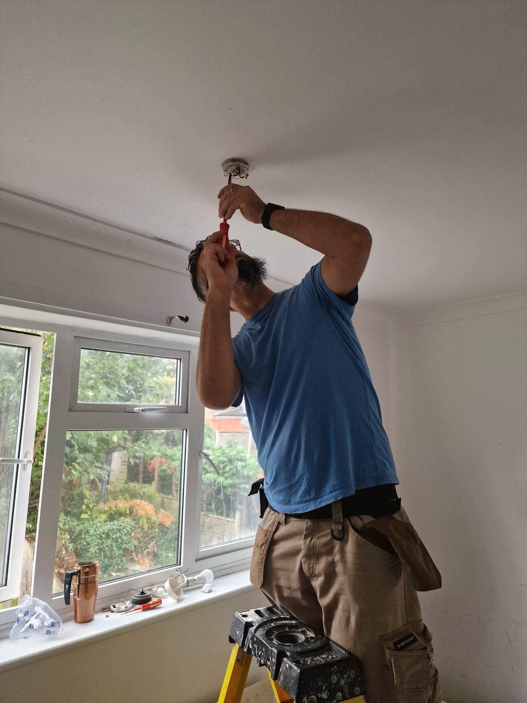 Arnie fitting a ceiling light while standing on a step ladder during a job