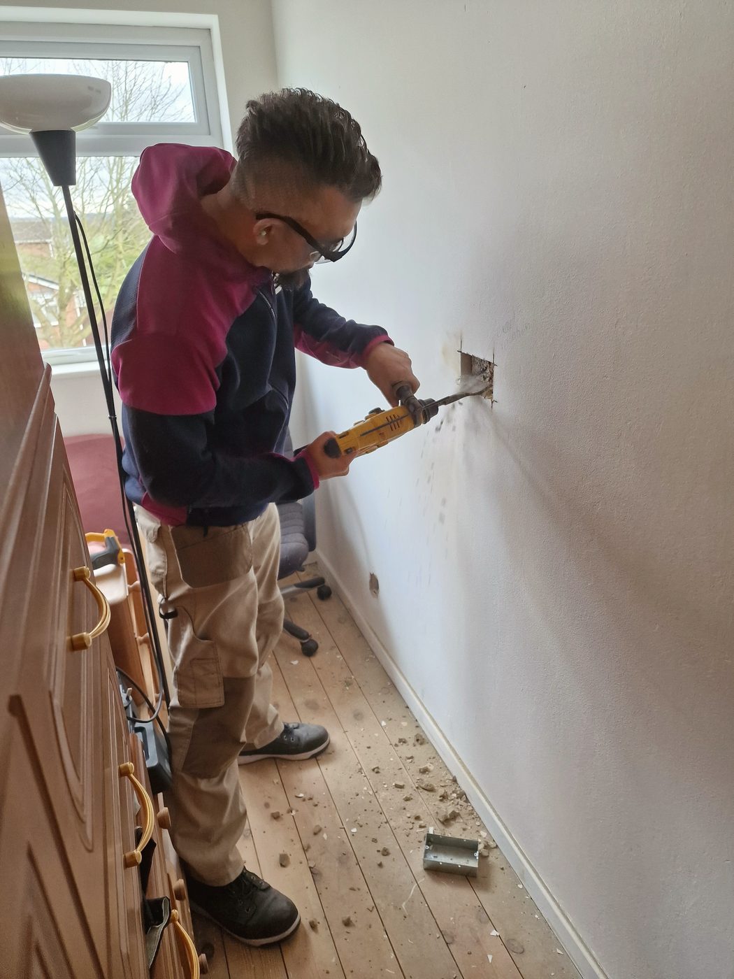 Arnis drilling a fixing into a wall during an installation