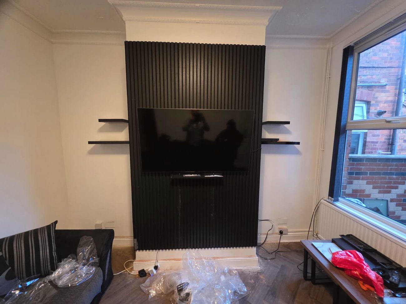 Black slatted feature wall with a mounted TV and floating shelves